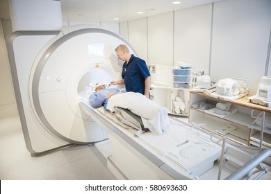Radiologist Putting Coil On Female Patient's Head Undergoing MRI