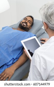 Radiologist Using Digital Tablet By Patient Lying On Bed