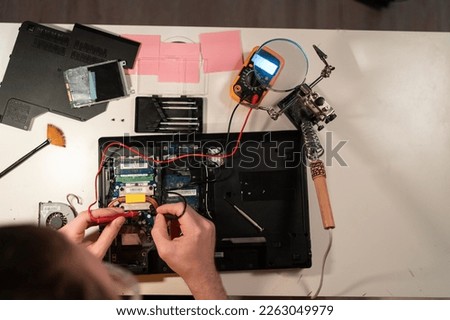 Radioman testing electric current in circuit board of disassembled laptop using multimeter. man measures voltage with ammeter on motherboard, top view. Copy space