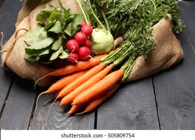 radish, kohlrabi and carrots on wooden background and jute bag
