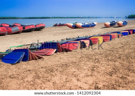 Rafts and oars on the bank near the river. Summer activity, team sport, rest. Blue sky, horizon. Sunny clear day.