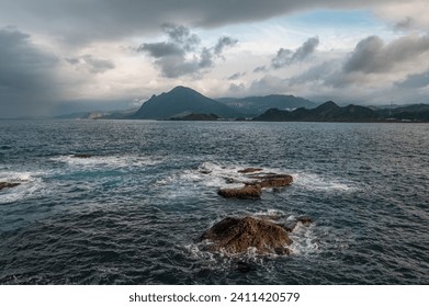 Rage waves of the ocean splashed on the rocks, Keelung mountain  in the background, in Keelung city, Taiwan.