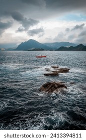 Rage waves of the ocean splashed on the rocks, Keelung mountain  in the background, in Keelung city, Taiwan.