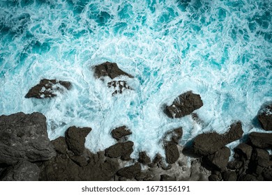 Raging Blue Ocean Waves Break On Rocks With Foam On The Water, Top View