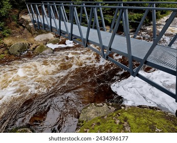 raging elements of water in a mountain river. the damaged and torn down wooden mast was washed away by the flood and crushed against the rocks. the new metal durable bridge withstands the waves of the
