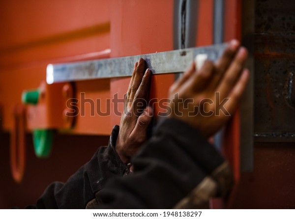 Rail car-building plant. Worker with steel ruler\
marking train car with chalk. No face, hand only. Low depth of\
field. Left hand in focus.