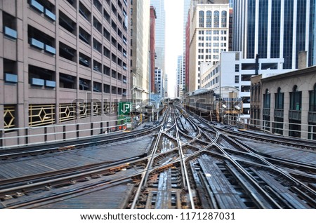 Rail track junction interchange in urban area in between buildings on left and right with platform on the right.
