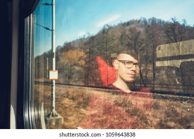 Rail Transportation In Sunny Day. Pensive Young Man Traveling Seen Though Train Window With Reflection. 