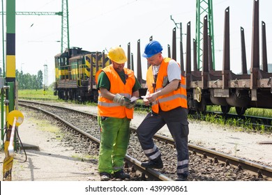 Железнодорожные работники координируют погрузку грузов на транспортный поезд по рельсам. Железнодорожные работники в безопасности запад и шлем говорят о инструкции.