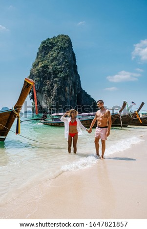 Railay Beach Krabi Thailand, couple walking in the morning on the beach with tropical cliffs and long tail boats on the background at the Island of Railay beach Krabi