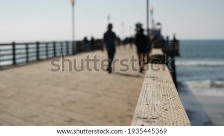 Railings of old wooden pier, people walking on waterfront boardwalk, Oceanside beach atmosphere, California coast USA. Defocused seascape, pacificocean water waves. Los Angeles summertime vacations.