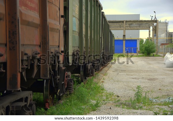Railroad cars in a dead end at an old\
abandoned factory at the blue gate of the\
warehouse.