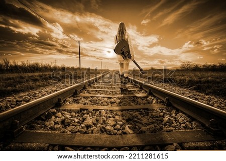 Railroad line girl standing with guitar on track sepia.