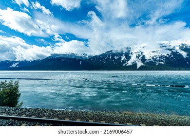 Railroad track on the frozen lake shore. Mountain range over blue sky white clouds. Canadian Rockies, Jasper National Park.