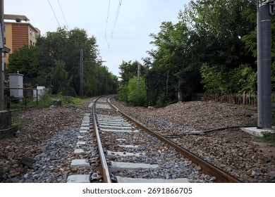 Railroad track passing through a patch of trees between buildings in an italian town on a cloudy day