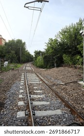 Railroad track passing through a patch of trees between buildings in an italian town on a cloudy day