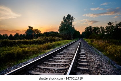 Railroad track in rural landscape with grass field and trees at sunset in Rastatt, Germany.