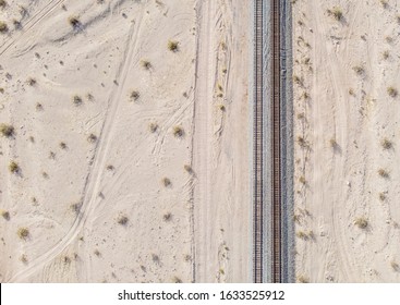 Railroad tracks run in a straight line across a flat desert landscape.  Seen from above looking straight down at rail way.  - Powered by Shutterstock