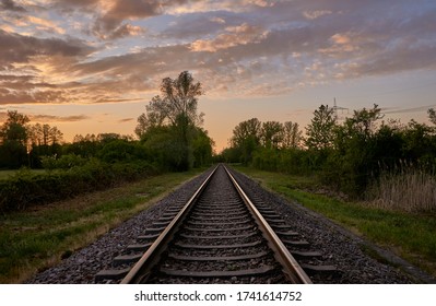 Railroad tracks in rural landscape against beautiful setting sun and cloudy sky in Rastatt, Germany.  - Powered by Shutterstock