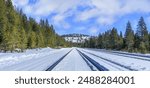 railroad tracks in the snow leading up through the center of the shot to a snowy mountain surrounded by trees.