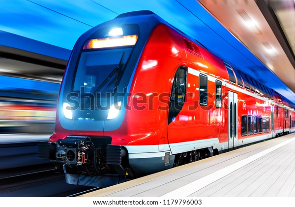 Railroad travel and railway transportation\
industrial concept: modern red high speed electric passenger\
commuter double deck train at the illuminated station platform at\
night with motion blur\
effect