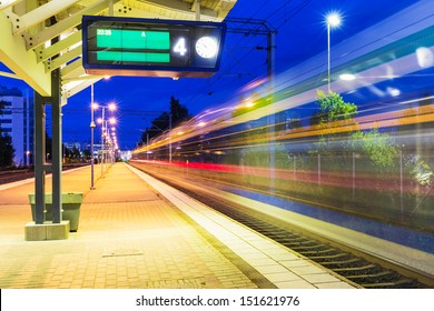 Railroad Travel And Transportation Industry Business Concept: Summer Night View Of High Speed Passenger Train Departing From Railway Station Platform With Motion Blur Effect