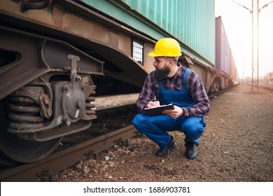 Railroad Worker Checking Up Wheels And Braking System Of Freight Train. Safety Inspector Or Maintenance Engineer Checking Rail Tracks At Station.