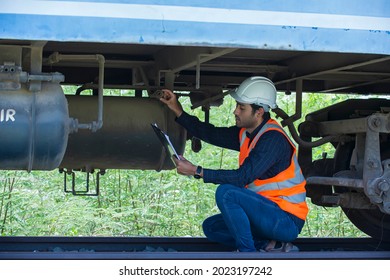 Railroad Worker Checking Up Wheels And Braking System Of Freight Train. Safety Inspector Or Maintenance Engineer Checking Rail Tracks At Station.