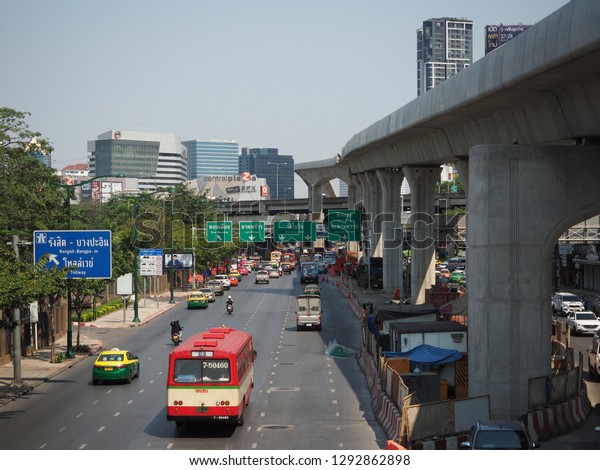 Railway of electric train and many building in the\
city landscape view with traffic on the road at January Bangkok\
Thailand 2019