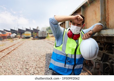 A Railway Engineer Or Rail Transport Technician Wearing A Green Safety Vest Is Standing To Rest Or Working Outdoors Beside A Freight Train On A Hot And Sunny Day.