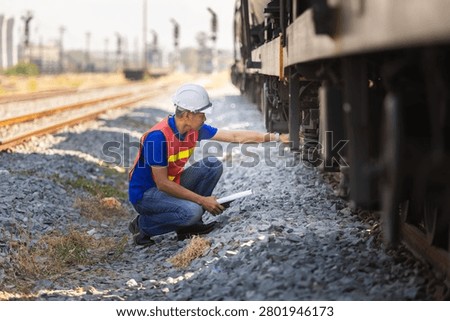 Railway inspector checking freight train suspension and wheel assembly at railyard, Engineer in hardhat and safety vests performing maintenance inspection on cargo train equipment
