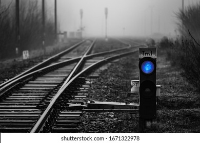 Railway signal with blue light with railroad junction disappearing in mist, monochrome image with blue colour