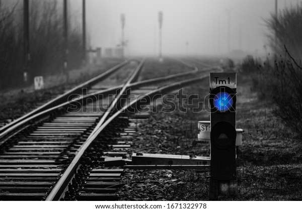 Railway signal with\
blue light with railroad junction disappearing in mist, monochrome\
image with blue colour