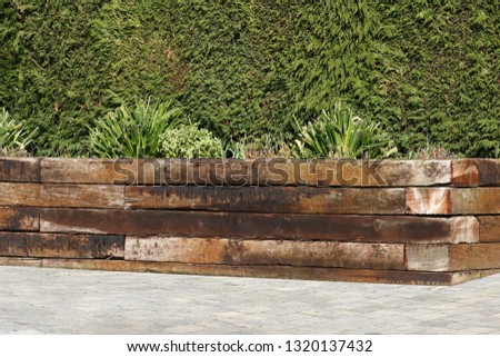 Railway sleepers forming raised bed with green shrubs against hedge background

