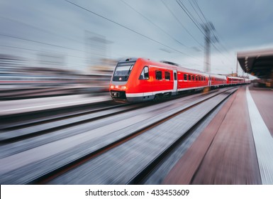 Railway Station With Modern High Speed Red Passenger Train At Sunset In Nuremberg, Germany. Railroad With Motion Blur Effect Vintage Toning. Industrial Landscape