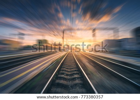 Railway station with motion blur effect. Blurred railroad. Industrial conceptual landscape with blurred railway station, buildings, blue sky with colorful clouds and sun. Railway track. Background