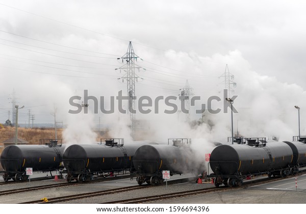 Railway\
tanker cars used to transport petroleum products. Several card\
visible. Fog or smoke rises from the cars. The cars are in the yard\
that loads them. Identifying marks\
removed.