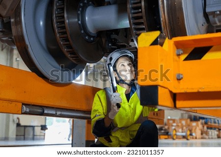 Railway technician engineer woman hold light stick to check and fix the problem under electric train infor working at maintenance plant of sky train or depot.