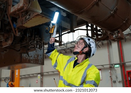 Railway technician engineer woman hold light stick to check and fix the problem under electric train infor working in maintenance plant of sky train or train depot.