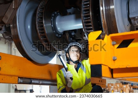 Railway technician engineer woman holds a light stick to check and fix the problem under an electric train for working at a sky train or depot maintenance plant. transportation and transport