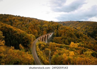 A railway track curving through an autumn forest with a bridge spanning a valley. The vibrant fall colors of the trees create a stunning contrast against the overcast sky.

 - Powered by Shutterstock