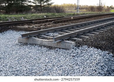 a railway track section under construction, resting on new grey gravel ballast with concrete sleepers.