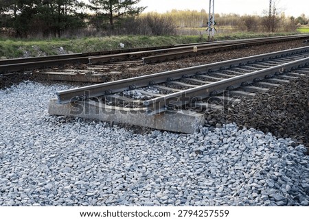 a railway track section under construction, resting on new grey gravel ballast with concrete sleepers.