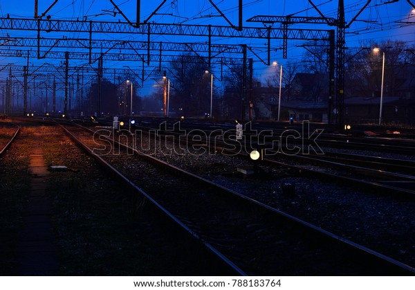 Railway tracks, semaphores, lights in the evening\
and light fog\
