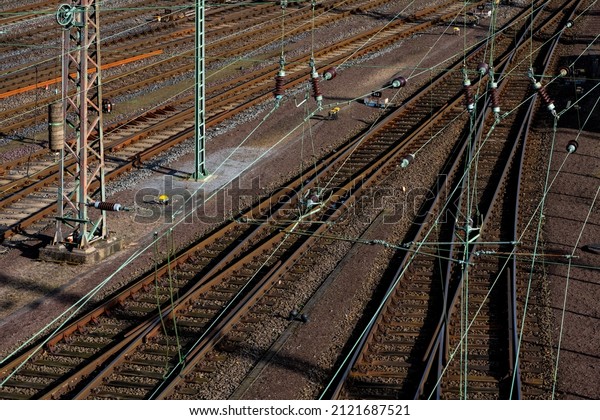 Railway tracks with switches at a big freight\
station shunting yard in Hagen-Vorhalle  Germany. Overhead lines,\
thresholds, power poles and brown gravel and rusty background.\
Green copper wires.
