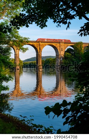 Railway Viaduct crossing Ruhr river in Herdecke Germany. Historic brick stone construction and sight with big tall arches on the branch line from Hagen to Dortmund reflecting in the water with train.