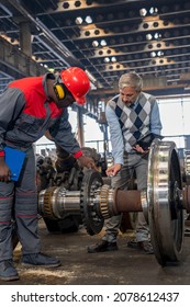 Railway Wheel Set Maintenance At Train Factory. Production Manager Talking To African American Worker In Protective Workwear Next To Train Wheels. Area For Maintenance, Repair And Service Of Trains.