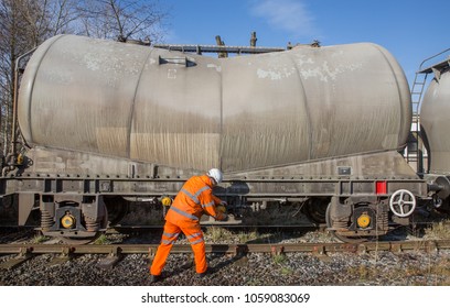 A Railway Worker In Hi Viz Clothing Repairing A Tanker Wagon At The Rail Side.