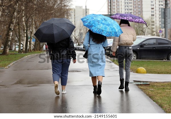 Rain in city, three girls\
with umbrellas walking down a street. Rainy weather, spring female\
fashion