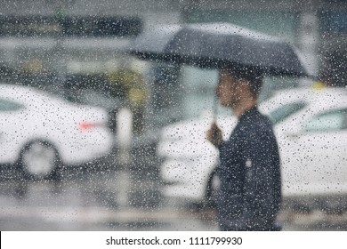 Rain In City. Young Man Holding Umbrella Walking In The Street. Selective Focus On  Raindrops On The Window.